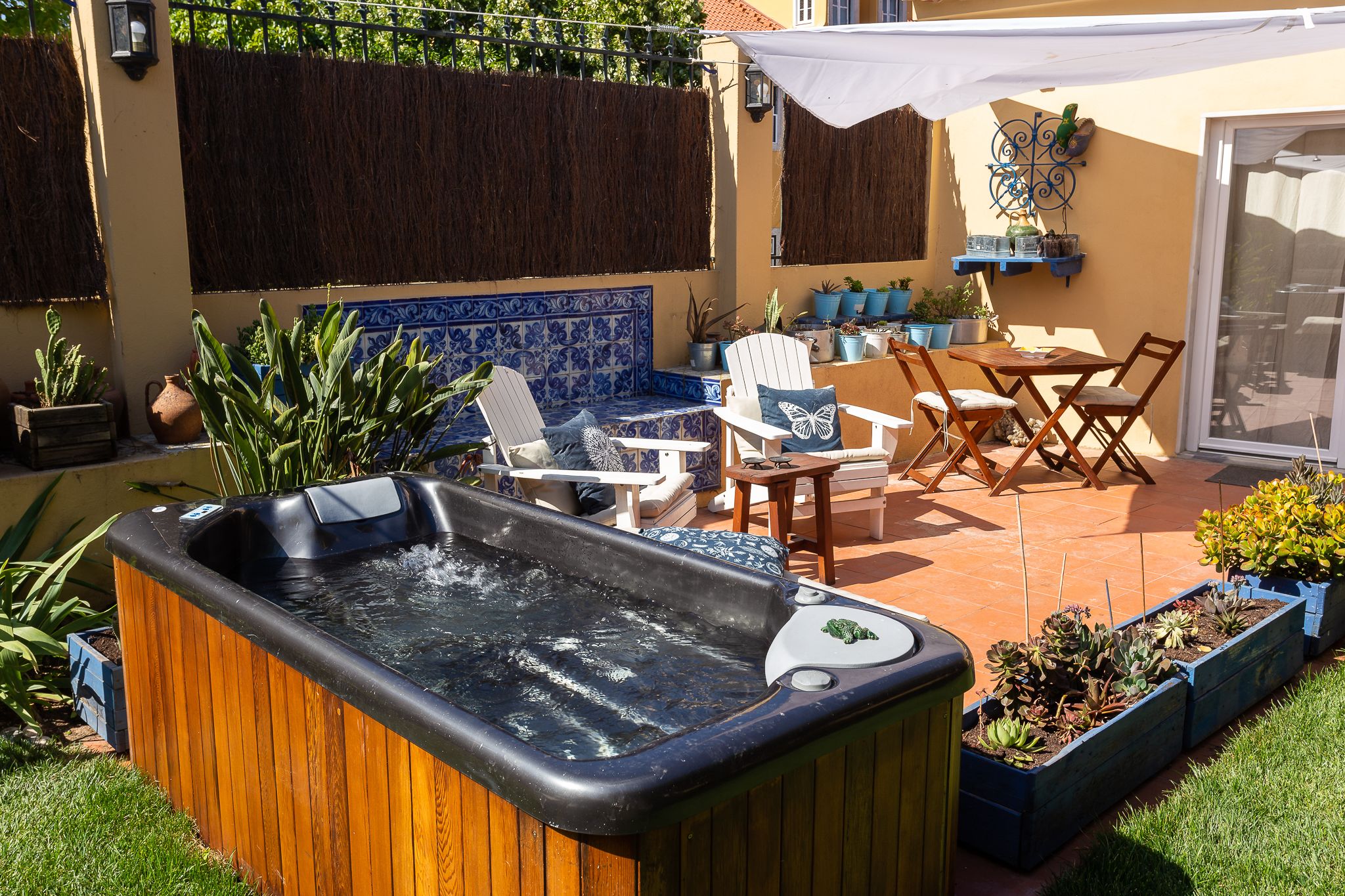 Een jacuzzi in een achtertuin met tuinmeubilair, potplanten en een betegelde muur.