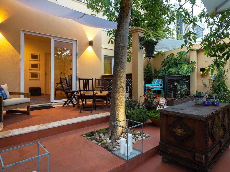 Un patio al aire libre con una mesa de madera, sillas y un pequeño jardín con plantas en macetas.