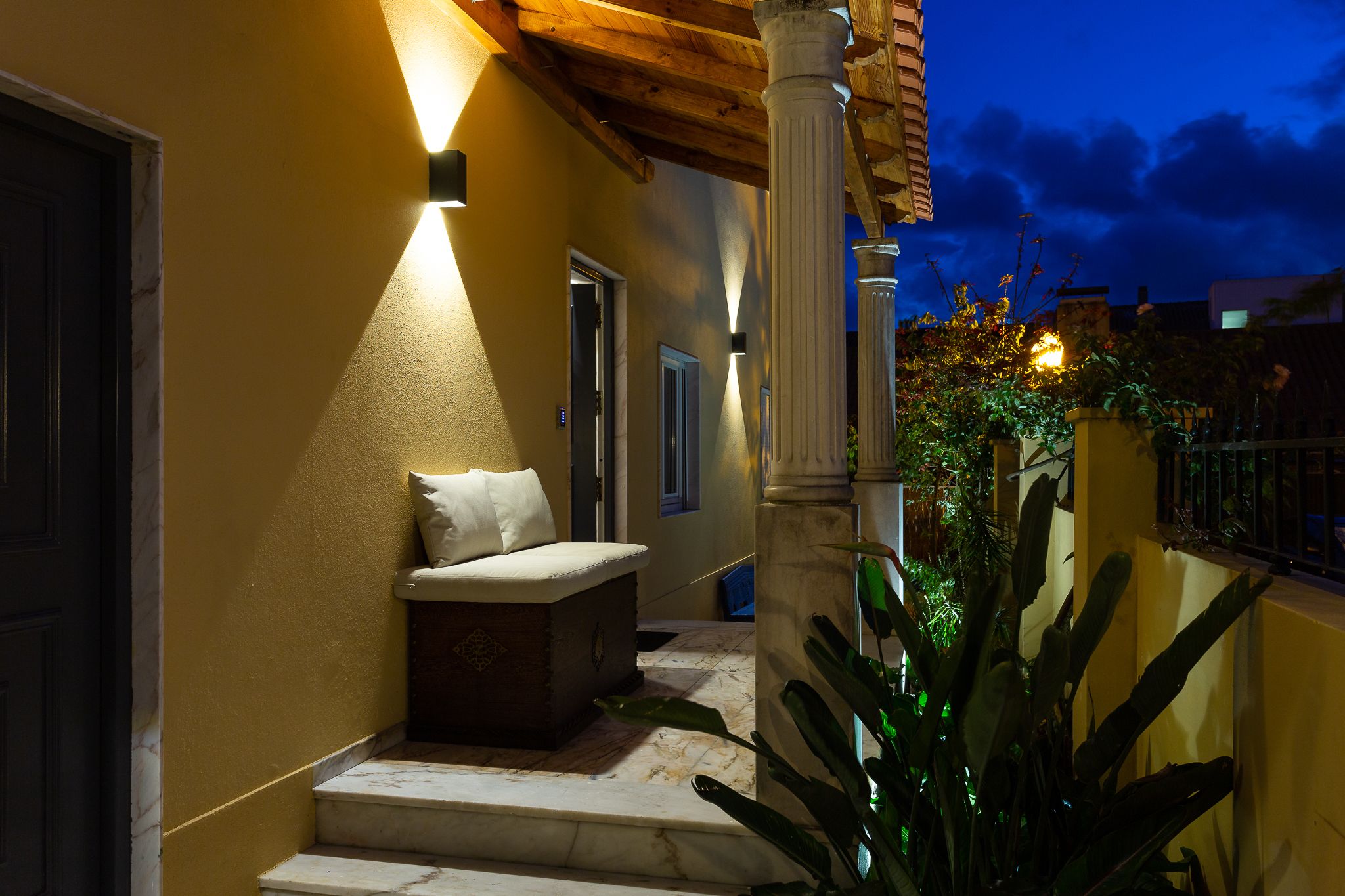 A well-lit outdoor area with a bench, a column, and a door leading to another room.