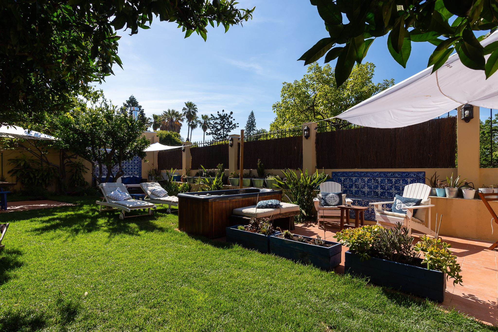 Eine Terrasse mit Lounge-Möbeln, einem Holz-Pflanzkübel und einer gefliesten Wand.