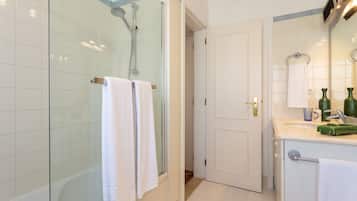 Une salle de bain moderne avec une douche à parois de verre, des carreaux blancs, un lavabo avec un miroir et une porte donnant sur une autre pièce.