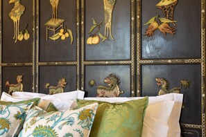 A room with a bed, pillows, and a wall decorated with animal and fruit carvings.