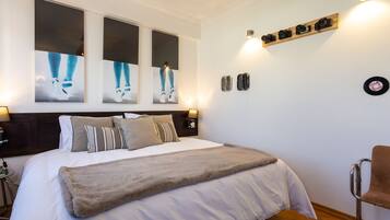 Un dormitorio ordenado con una cama grande, una mesita de noche, una silla y lámparas fijadas a la pared.