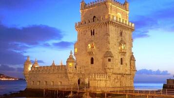 A historic stone castle with multiple towers and a fortified wall, situated by a calm body of water.