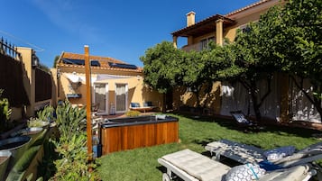 Un patio trasero con jacuzzi, sillones de descanso y una zona de estar con pérgola.