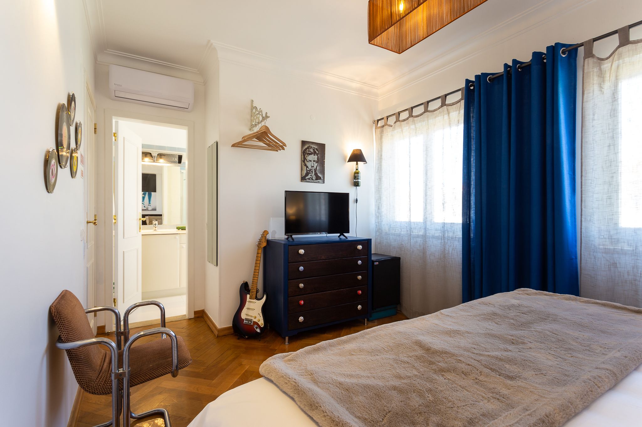 A bedroom with a bed, a dresser, a TV, and a guitar.