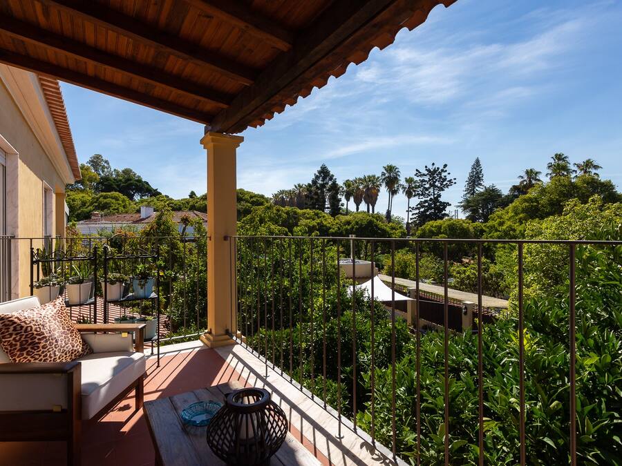 Uma varanda com pérgola de madeira, um sofá com almofada estampada de leopardo e plantas em vasos.