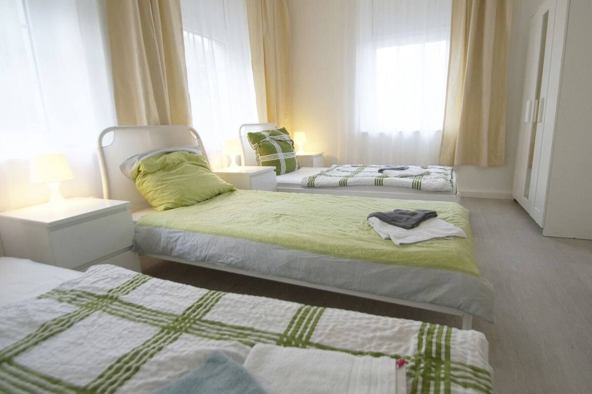 A hotel room with two single beds, a nightstand with a lamp, and a window with curtains.