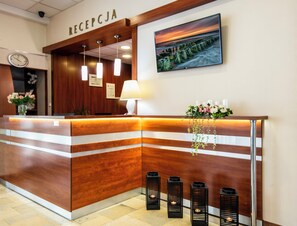 A reception desk with a wooden finish, a clock, a framed certificate, and a framed landscape painting. - INTERFERIE Cechsztyn w Ustroniu Morskim (Ustronie Morskie)