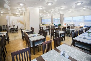 Un restaurante con varias mesas y sillas, una zona de cocina y ventanas amplias.