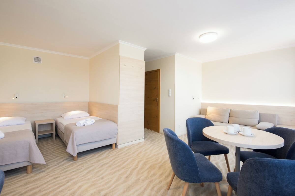 A hotel room with two single beds, a small table with chairs, and a sofa.