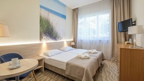 A hotel room with two beds, a desk, a chair, a TV, and a painting of a beach. - INTERFERIE Cechsztyn w Ustroniu Morskim (Ustronie Morskie)