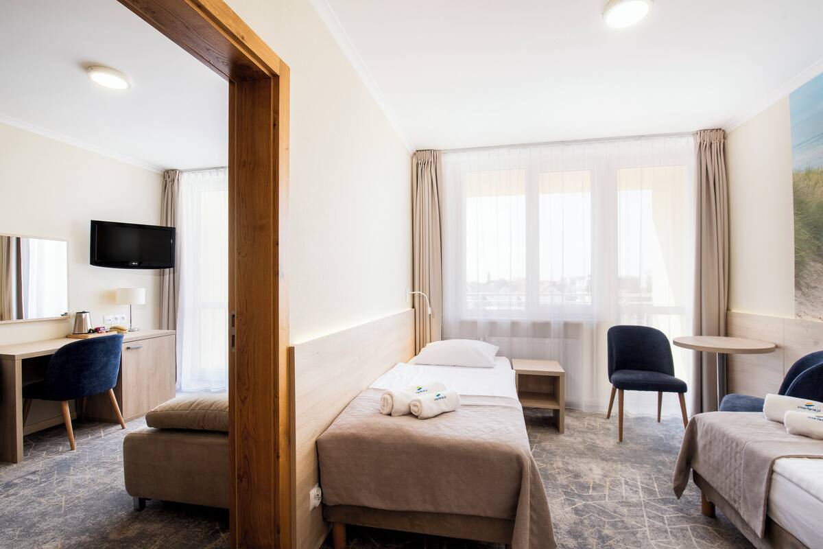 A hotel room with a bed, a desk, a chair, a TV, and a window with curtains.