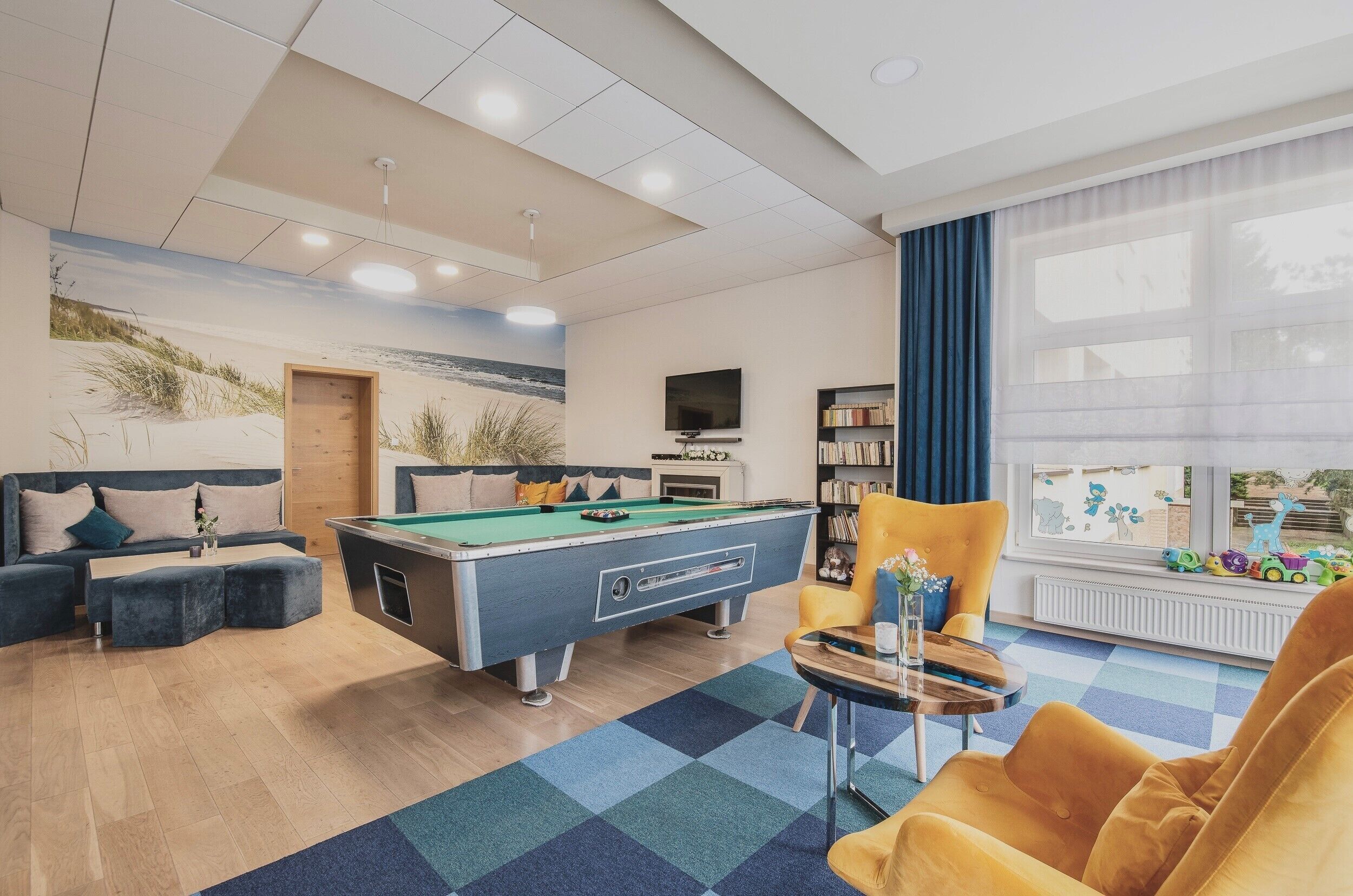 A room with a pool table, sofa, and a bookshelf.