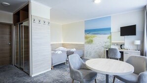 A hotel room with a bed, two bedside tables, a desk, a chair, a round table, a TV, and a beach view mural. - INTERFERIE Cechsztyn w Ustroniu Morskim (Ustronie Morskie)