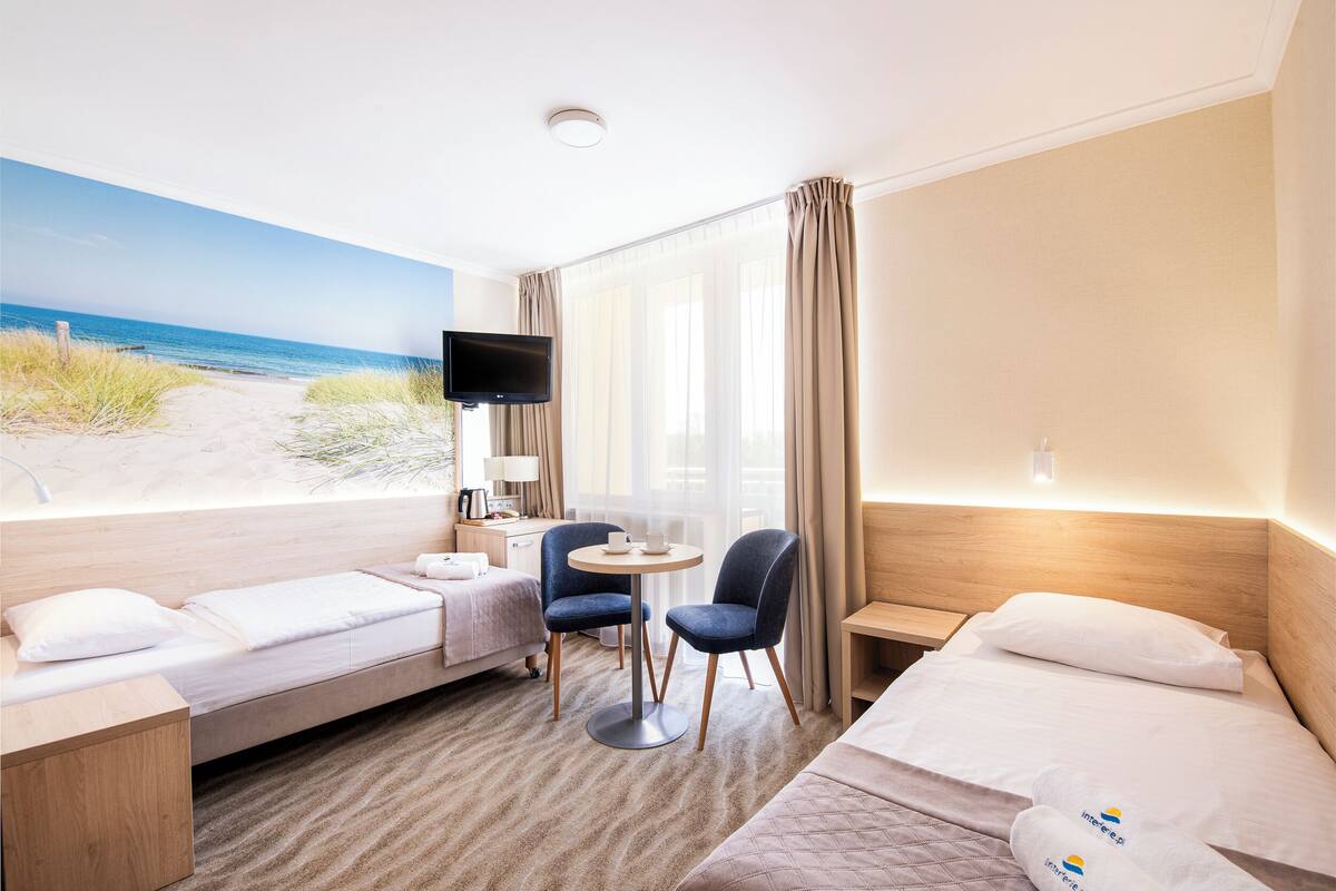 A hotel room with a bed, a desk, a chair, a TV, and a window with a beach view.