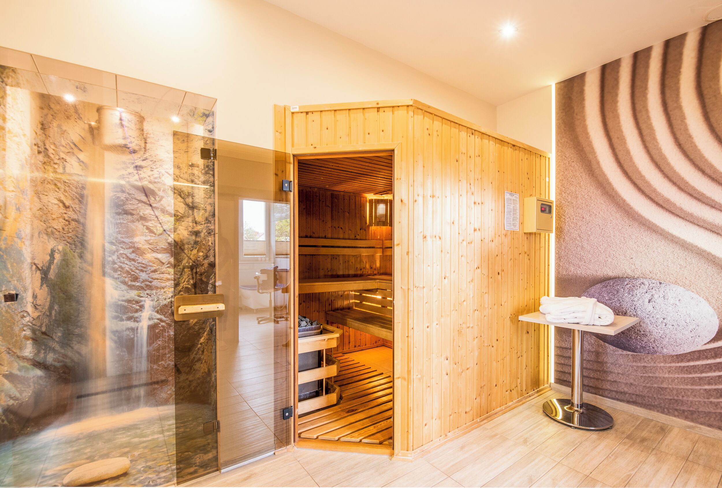Un cuarto de sauna con puerta de madera, cabina de ducha de vidrio y un mural de piedra en la pared.