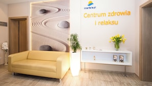 A reception area with a sofa, a wall with a logo and text, a plant, and a vase with flowers. - INTERFERIE Cechsztyn w Ustroniu Morskim (Ustronie Morskie)