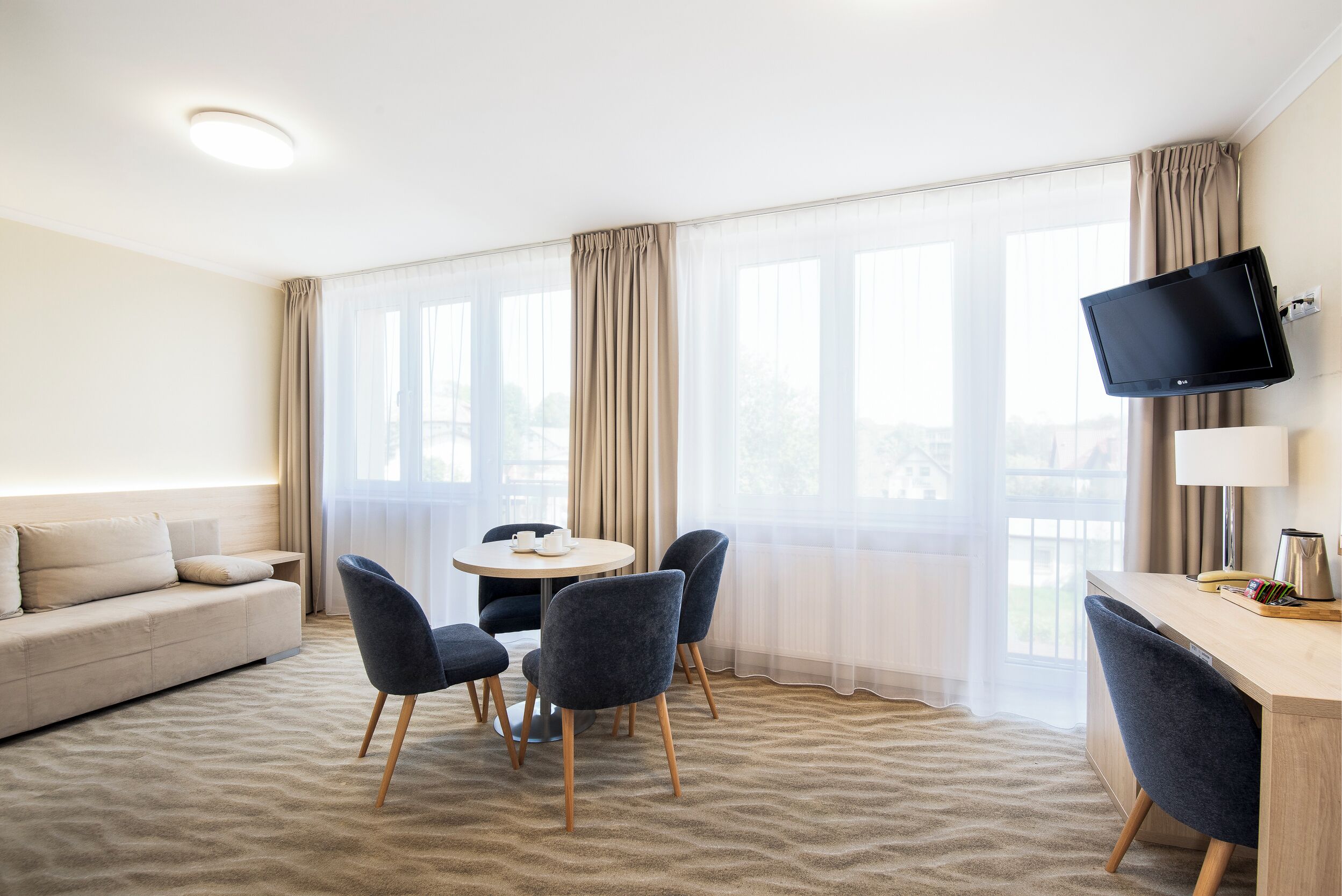 Habitación de hotel con sofá, mesa de comedor, sillas, televisor y escritorio.
