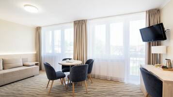 Habitación de hotel con sofá, mesa de comedor, sillas, televisor y escritorio.