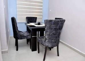 Enjoy meals in this dining area with a table and chairs, surrounded by a light blue wall and a window with horizontal blinds.