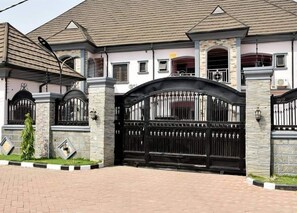 A large, gated residential property with a brick facade and a tiled roof. - Onim Luxury Apartments (Abuja)