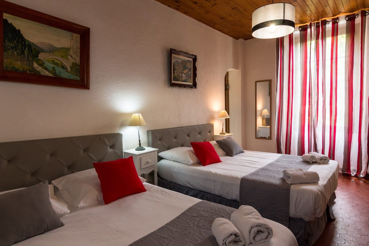 Una habitación de hotel con dos camas, techo de madera, un cuadro, una lámpara y un espejo.