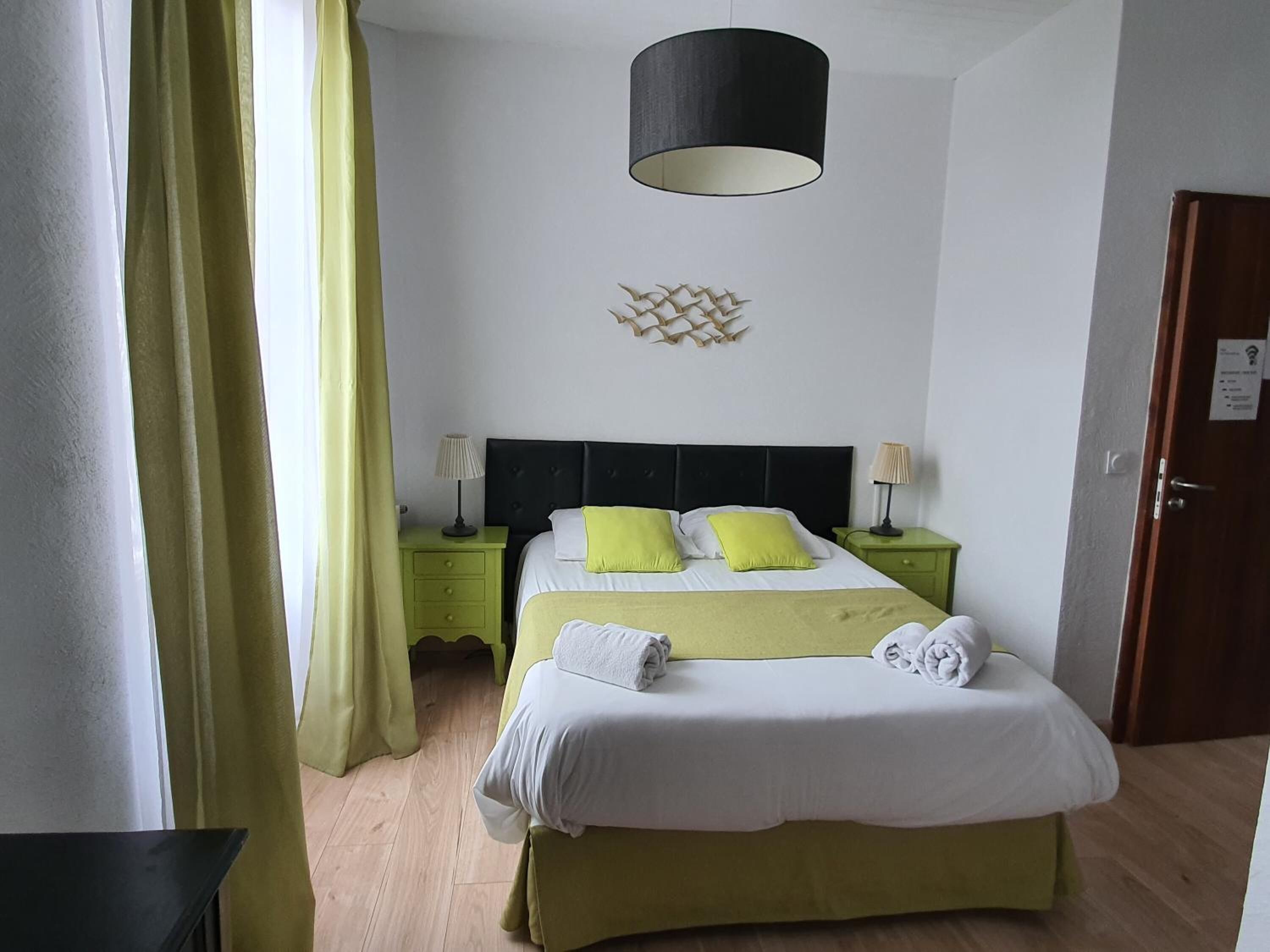 A hotel room with a bed, two bedside tables, a lamp, a wall decoration, and a door.