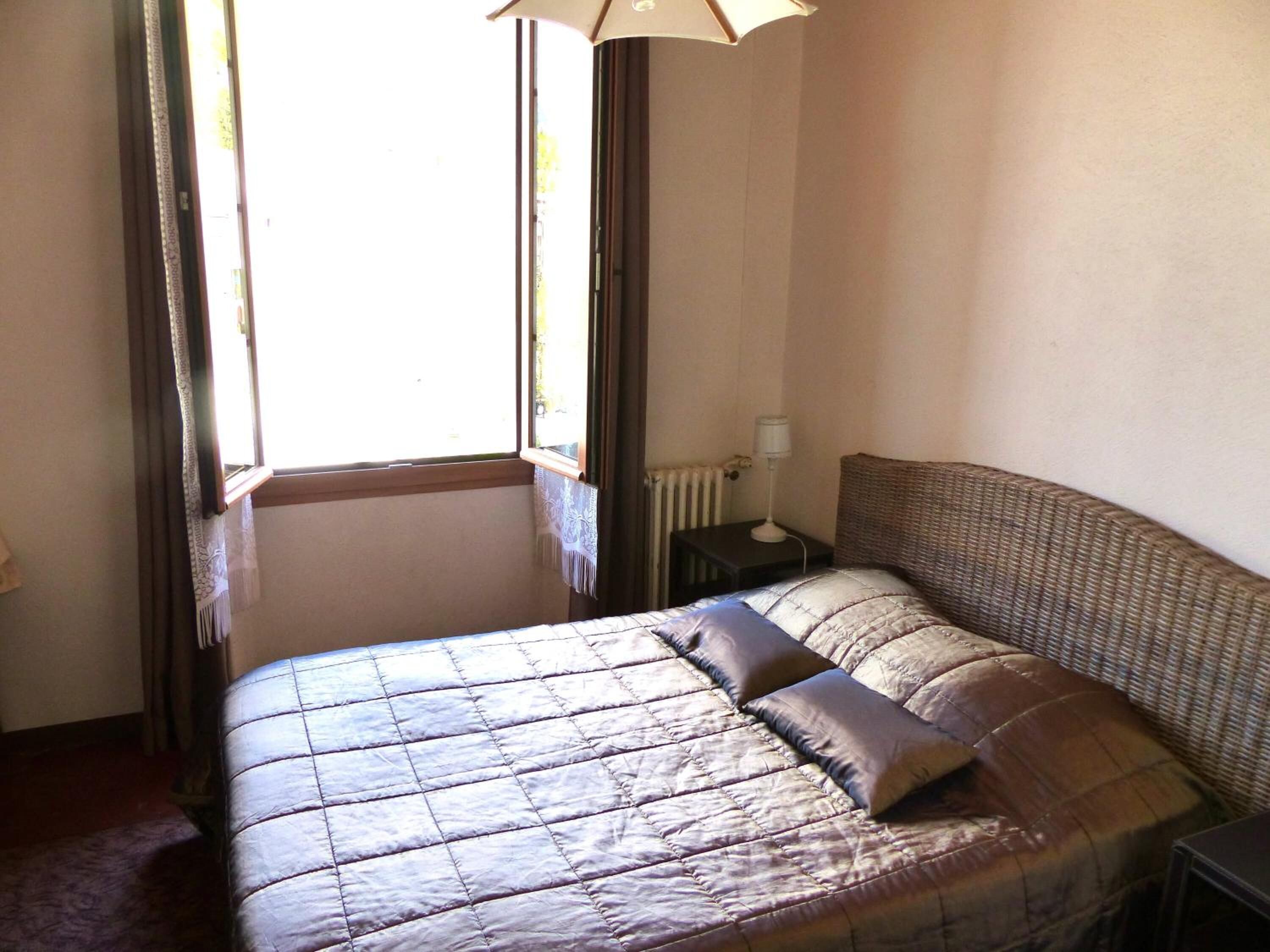 A bedroom with a bed, a nightstand, a lamp, and a window with curtains.