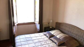 A bedroom with a bed, a nightstand, a lamp, and a window with curtains.