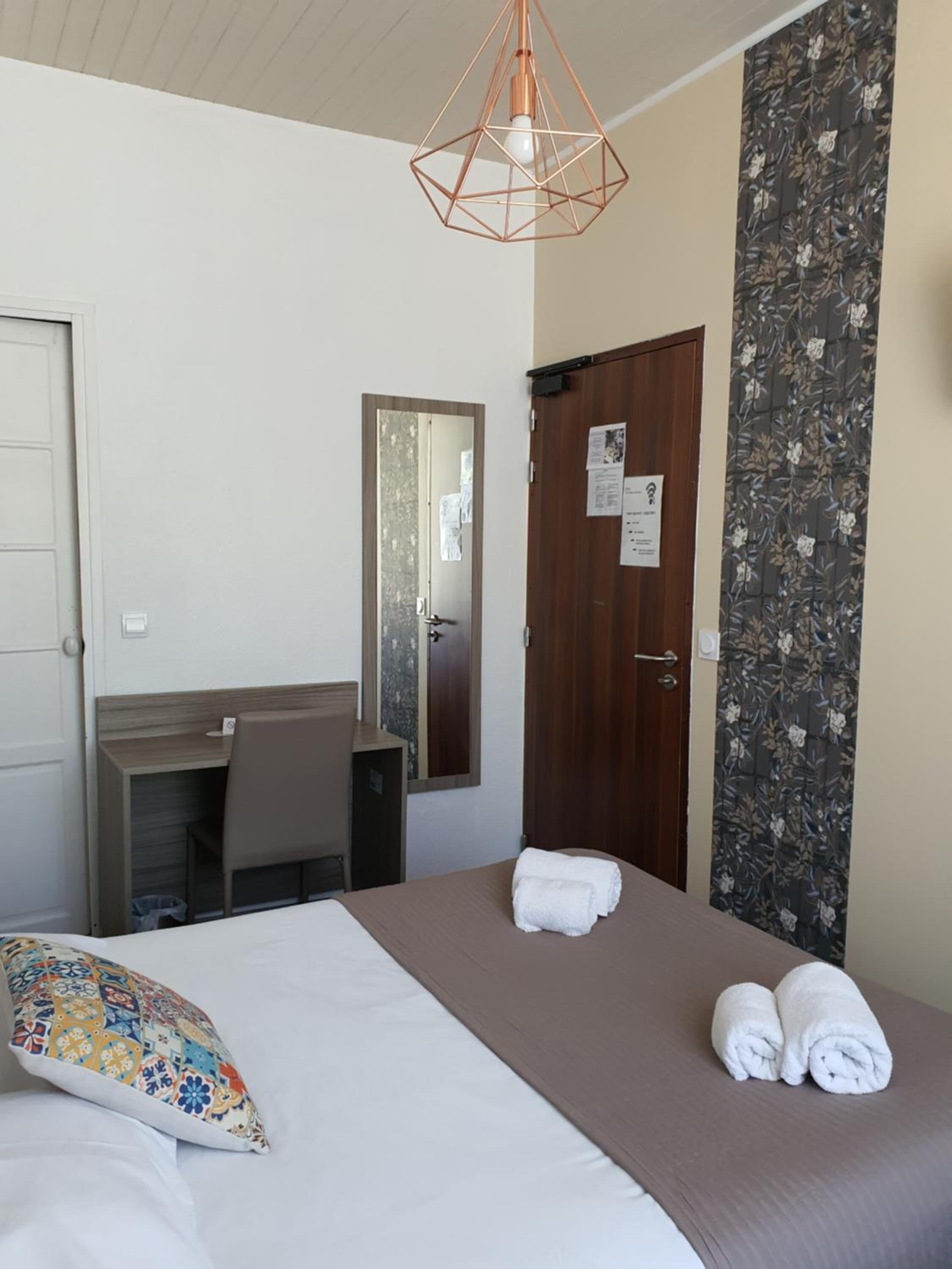 A hotel room with a bed, a desk, a chair, a wardrobe, and a hanging light fixture.