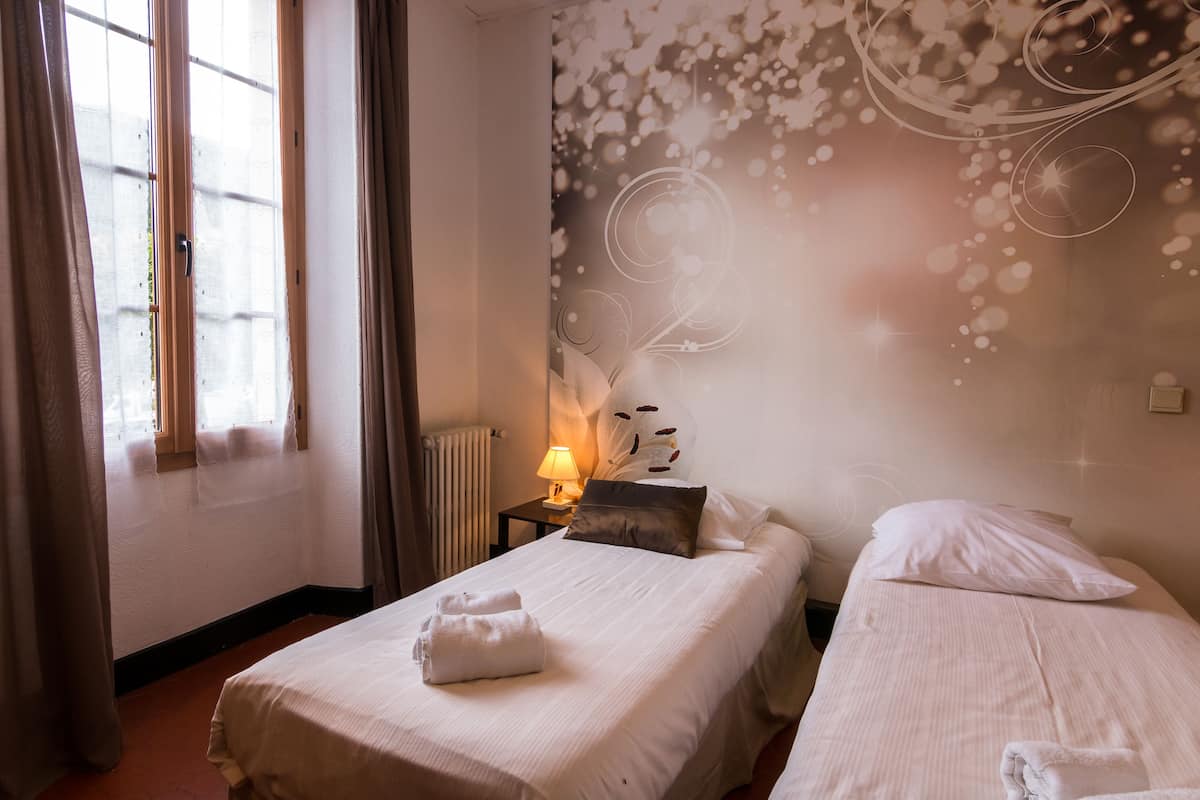 Habitación de hotel con dos camas, una mesita de noche con lámpara y un adorno en la pared.
