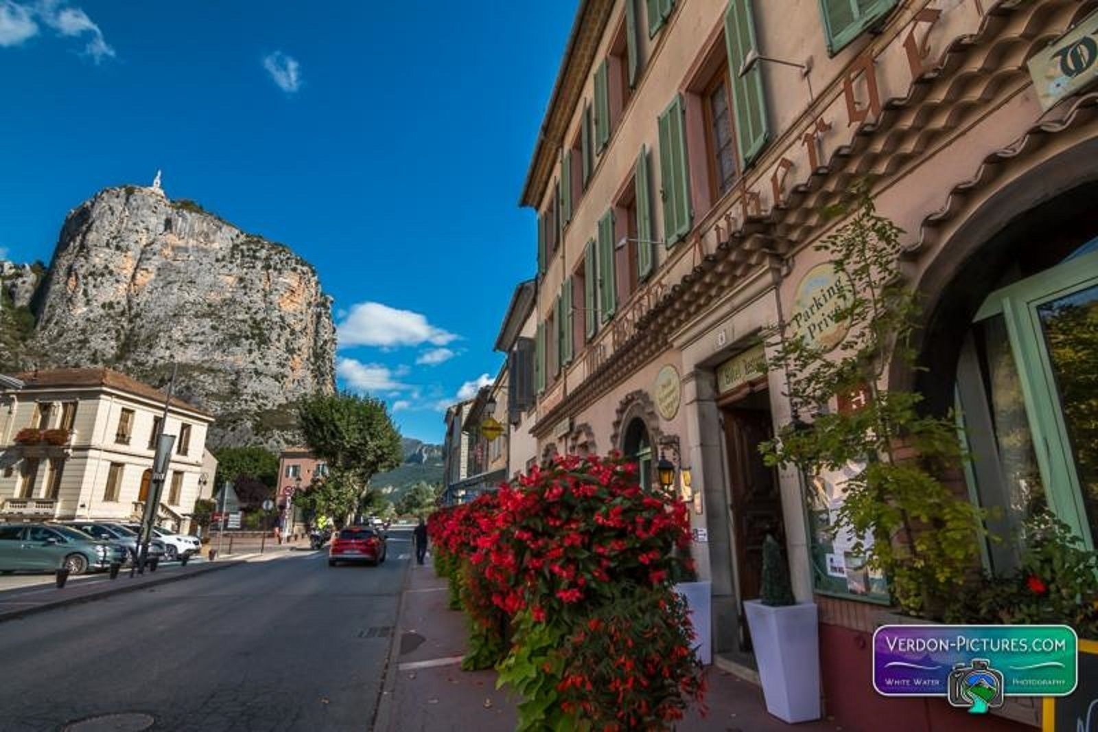 Une rue bordée d’immeubles, avec une formation rocheuse remarquable et des voitures garées.