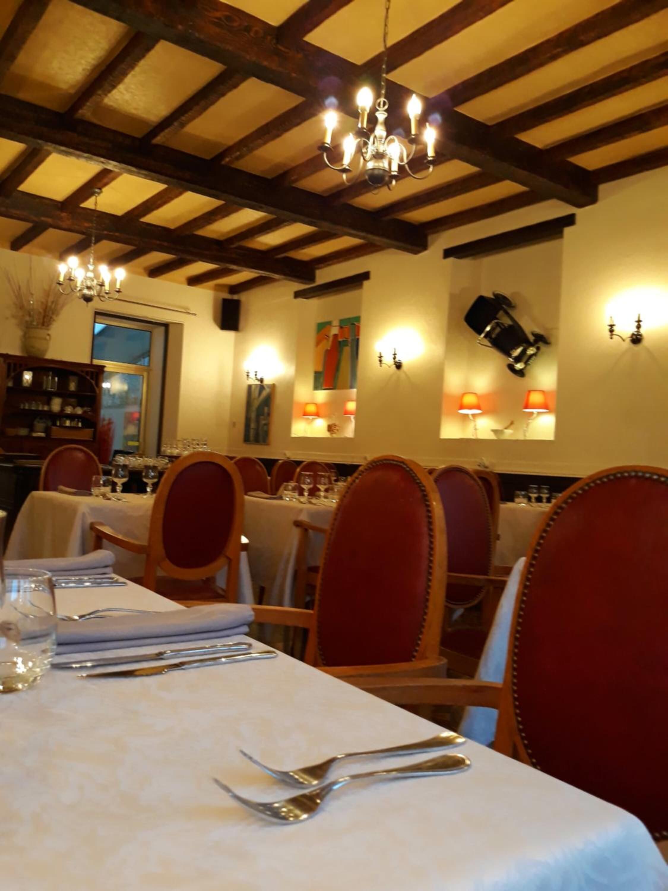A dining area with tables set for service, wooden chairs, and a chandelier.