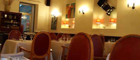 A dining area with tables set for service, wooden chairs, and a chandelier.
