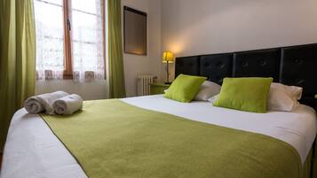 A neatly made bed with a green bedspread and two pillows, a nightstand with a lamp, and a window with green curtains.