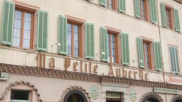 A building with multiple windows, a sign reading "Ma Petite Auberge," and outdoor seating with tables and chairs.