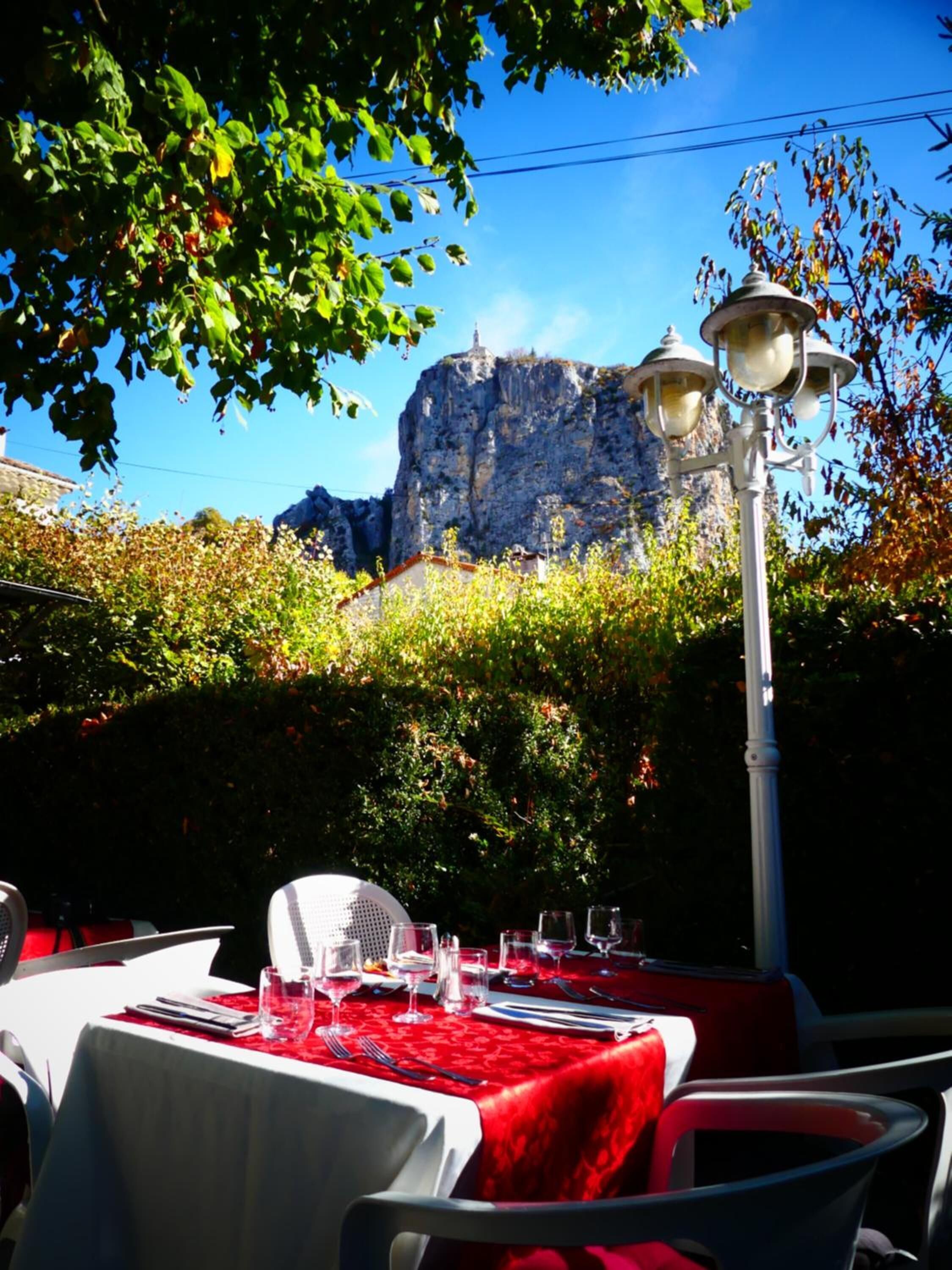 An outdoor dining area with tables set for two, a mountain backdrop, and a street lamp.
