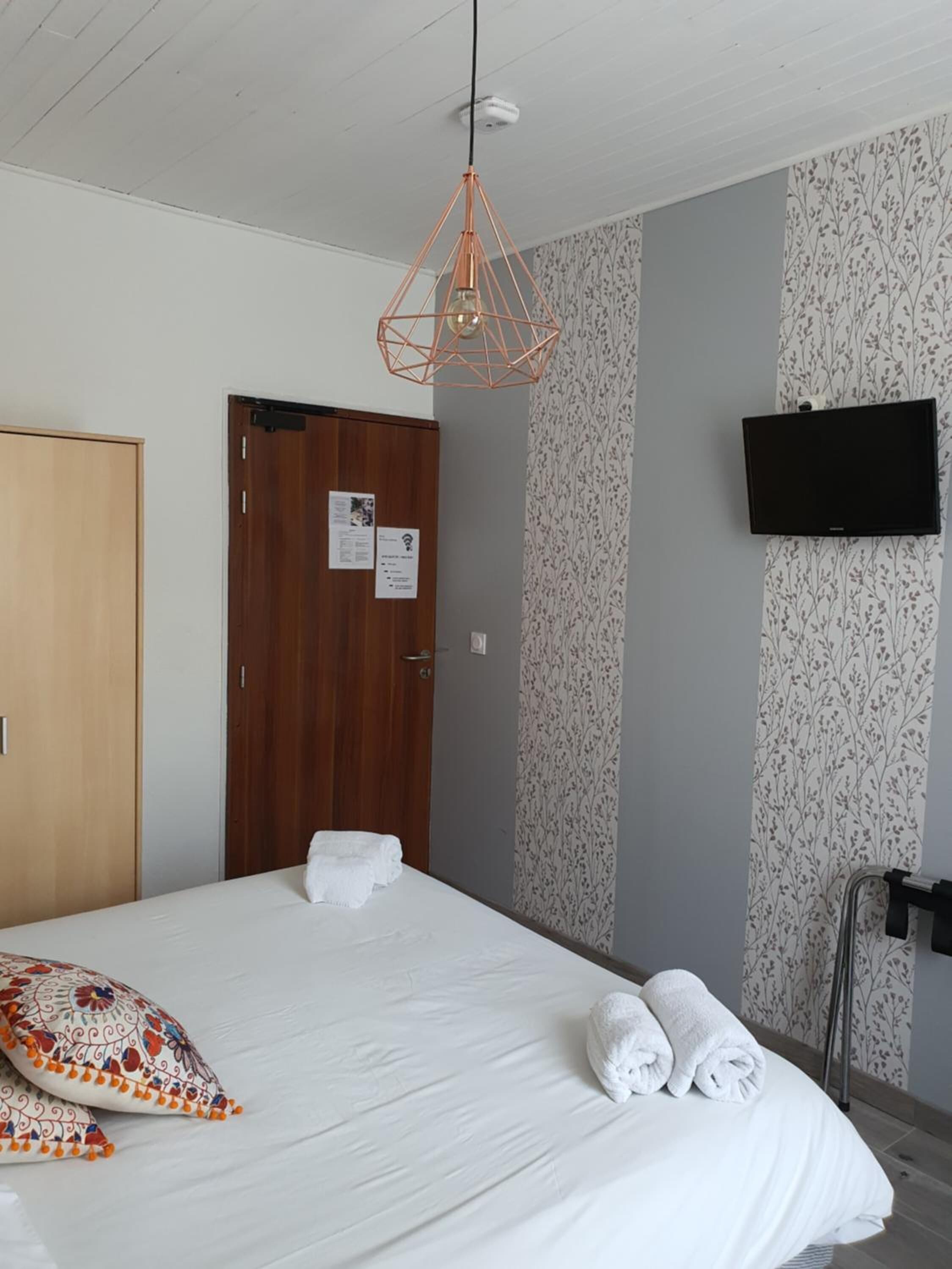 A hotel room with a bed, a wooden door, a wall-mounted TV, and a patterned wallpaper.