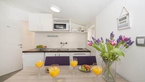 Una cocina moderna con armarios blancos, un microondas y un lavamanos. Hay cuatro vasos de jugo de naranja en la mesa, y un jarrón con flores.