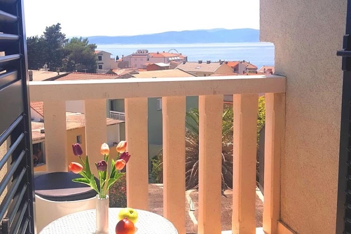 A balcony with a view of the sea, a table with a vase of flowers, and a chair.