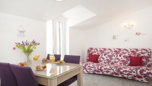Un comedor con una mesa de vidrio, sillas moradas, un sofá floral y una disposición para el desayuno con frutas y jugo.
