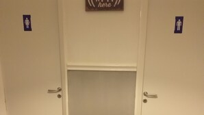 A hotel room with two doors, each marked with a female and male restroom symbol. A sign above the doors reads "Free Wi-Fi here." The floor is tiled with a stone pattern. - Hostel alexander (Naples)