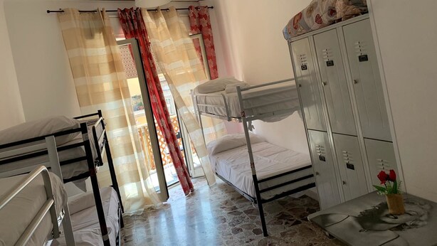 A dormitory room with bunk beds, a wardrobe, and a small table with a vase of flowers. - Hostel alexander (Naples)