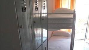 A bunk bed with a white mattress and pillows, a metal wardrobe with multiple compartments, and a stone-tiled floor. - Hostel alexander (Naples)