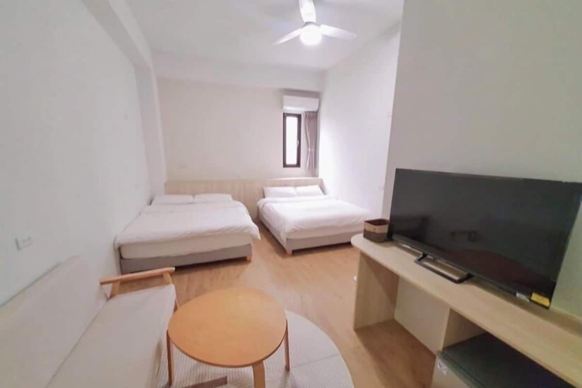 A small, clean room with two beds, a TV, and a ceiling fan.