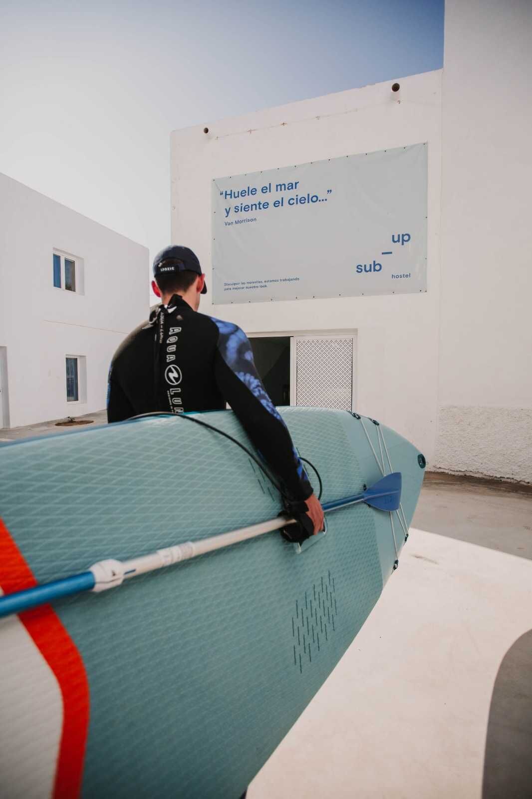 A person sitting on a surfboard in a room with a large poster on the wall.