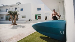 Un edificio moderno con piscina, palmeras y una persona cerca de la piscina.
