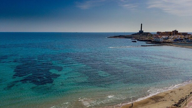 Vista costera con un faro, playa y edificios a lo largo de la orilla.