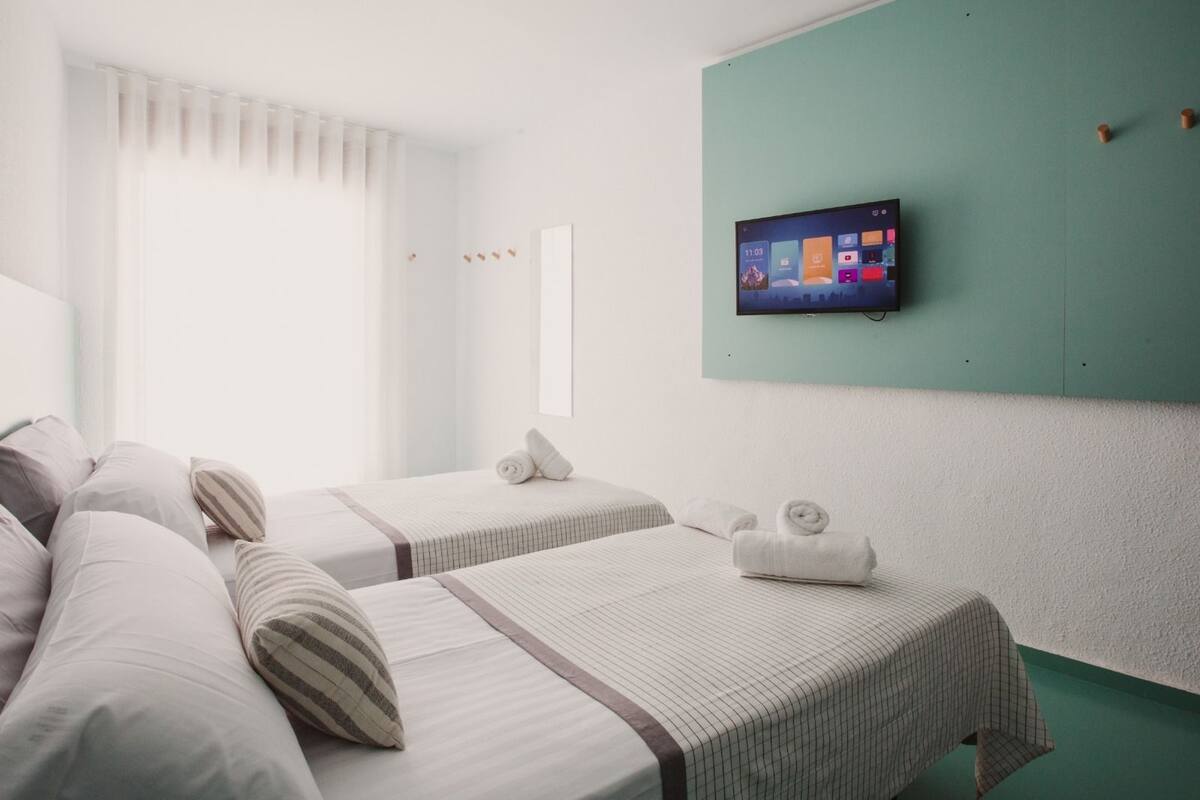 A hotel room with two beds, a TV mounted on the wall, and a window with curtains.
